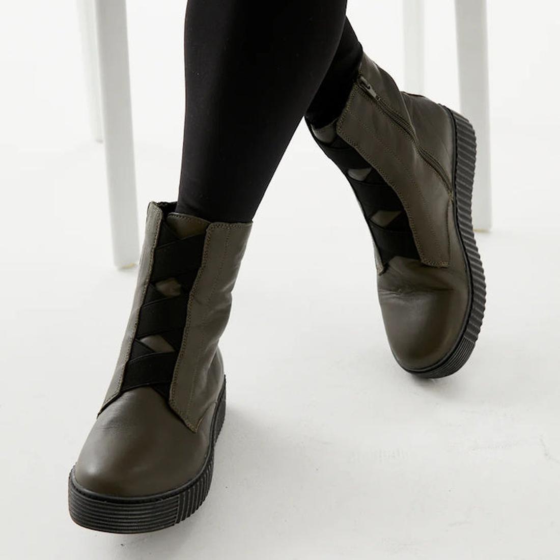 A parent models Alfie & Evie Womens Date Khaki Ankle Boots with comfy black platform soles and elastic straps, seated on a white chair. ksnz, 9353738178185, 9353738178192, 9353738178208, 9353738178215, 9353738178222, 9353738178239, 9353738178246