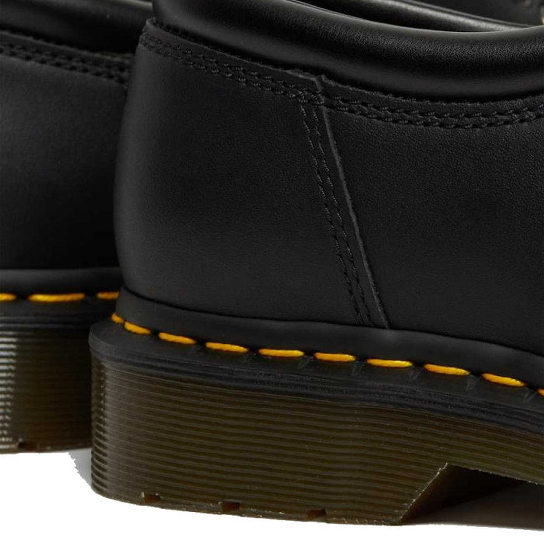 Close-up of the heel and stitching on Dr Martens 8053 Nappa Black Padded Collar Shoes, featuring yellow Goodyear welt stitching and a thick, ridged translucent sole. Another unisex shoe is partially visible in the background., 800090824704, 800090824728, 