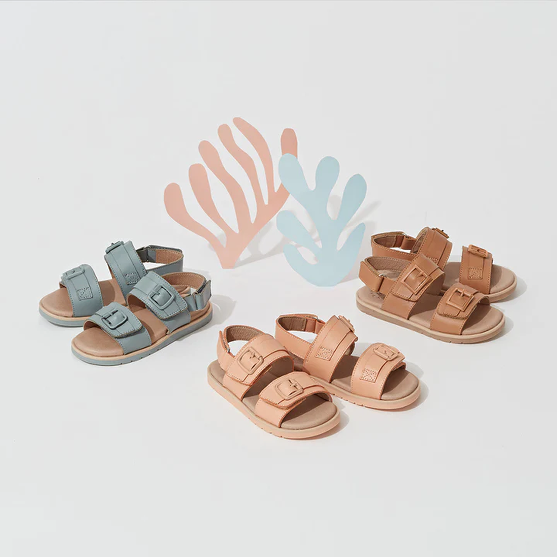 A pair of Pretty Brave Alex Leather Sandal in Seaform Blue (sizes 29-33, clearance, not returnable) is displayed on a white surface with pastel pink and blue abstract shapes; it features adjustable Velcro straps for comfort., 9421036357684, 9421036357691,
