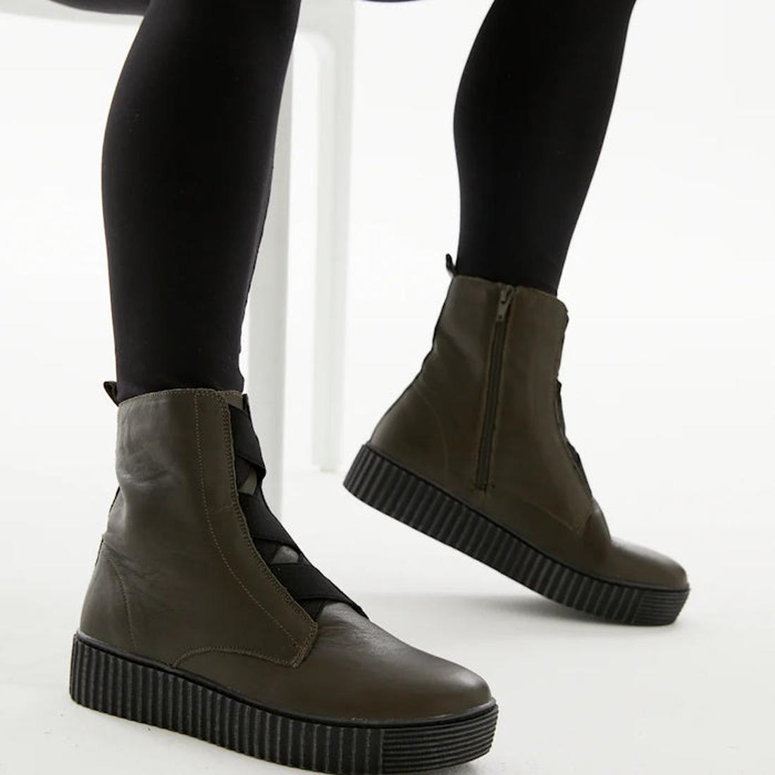 A woman stands by a white chair in black leggings and Alfie & Evie Womens Date Khaki Ankle Boots with comfy soles and side zips.  ksnz, 9353738178185, 9353738178192, 9353738178208, 9353738178215, 9353738178222, 9353738178239, 9353738178246