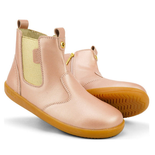 The Bobux Kid+ Jodphur Boot Rose Gold 830021 features rose gold leather, tan rubber soles, side zippers, and elastic panels for easy slip-on. These kids’ winter boots have a sleek finish and minimal stitching details.