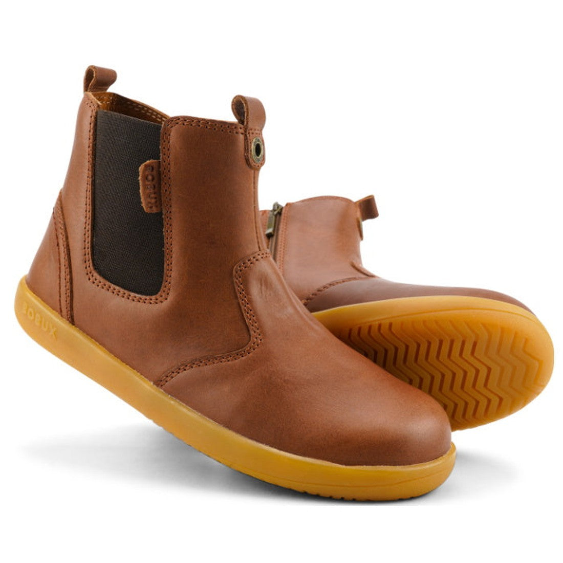 The Bobux Kid+ Jodhpur Leather Boot Toffee 830010E features brown leather, black elastic side panels, and yellow rubber soles, with one boot upright and the other angled to display the sole's tread pattern.