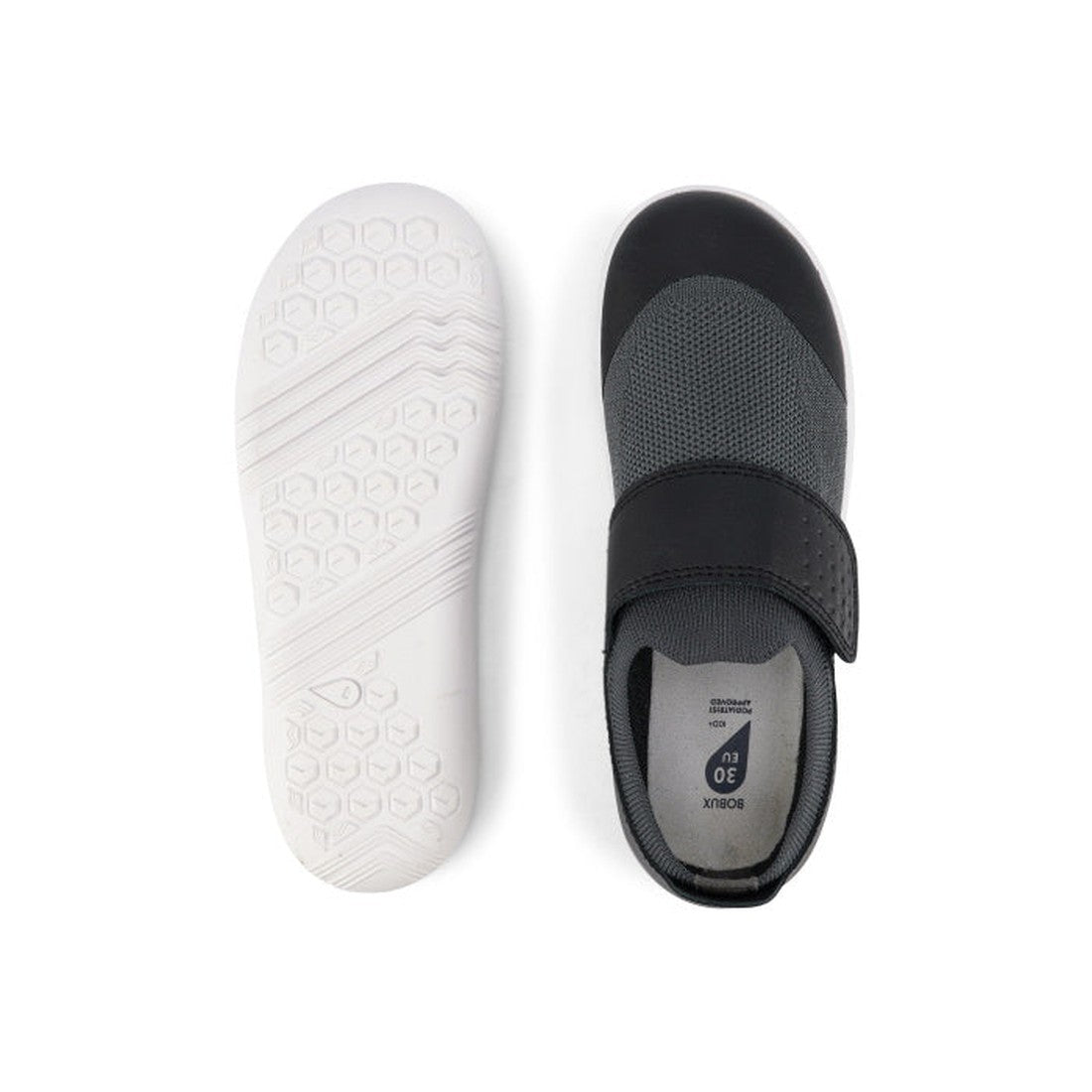 A pair of Bobux Kid+ Lo Dimension III Black 838604 children’s slip-on shoes with a wide hook-and-loop strap, shown top and bottom. The lightweight white sole has a hexagonal tread for flexible performance. CLEARANCE., 9420068517202, 9420068517219, 9420068
