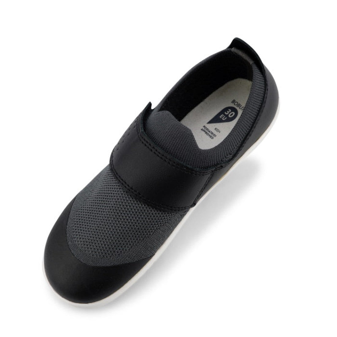 A single Bobux Kid+ Lo Dimension III Black 838604 CLEARANCE slip-on shoe with a mesh upper, elastic band across the top, lightweight flexible sole, and solid black toe cap is shown from above at an angle, highlighting its modern style., 9420068517202, 942