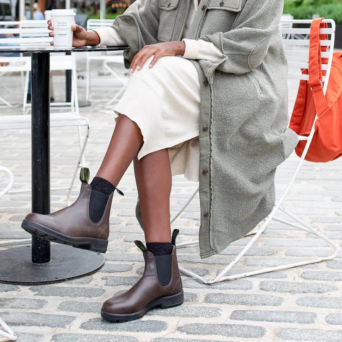 Enjoying coffee outdoors, this person wears comfortable Blundstone Chelsea Boot 2116 VEGAN Brown—easy pull-on style, durable sole.  ksnz, 9315891528689, 9315891528702, 9315891528726, 9315891528740, 9315891528764, 9315891528788, 9315891528801, 9315891528825