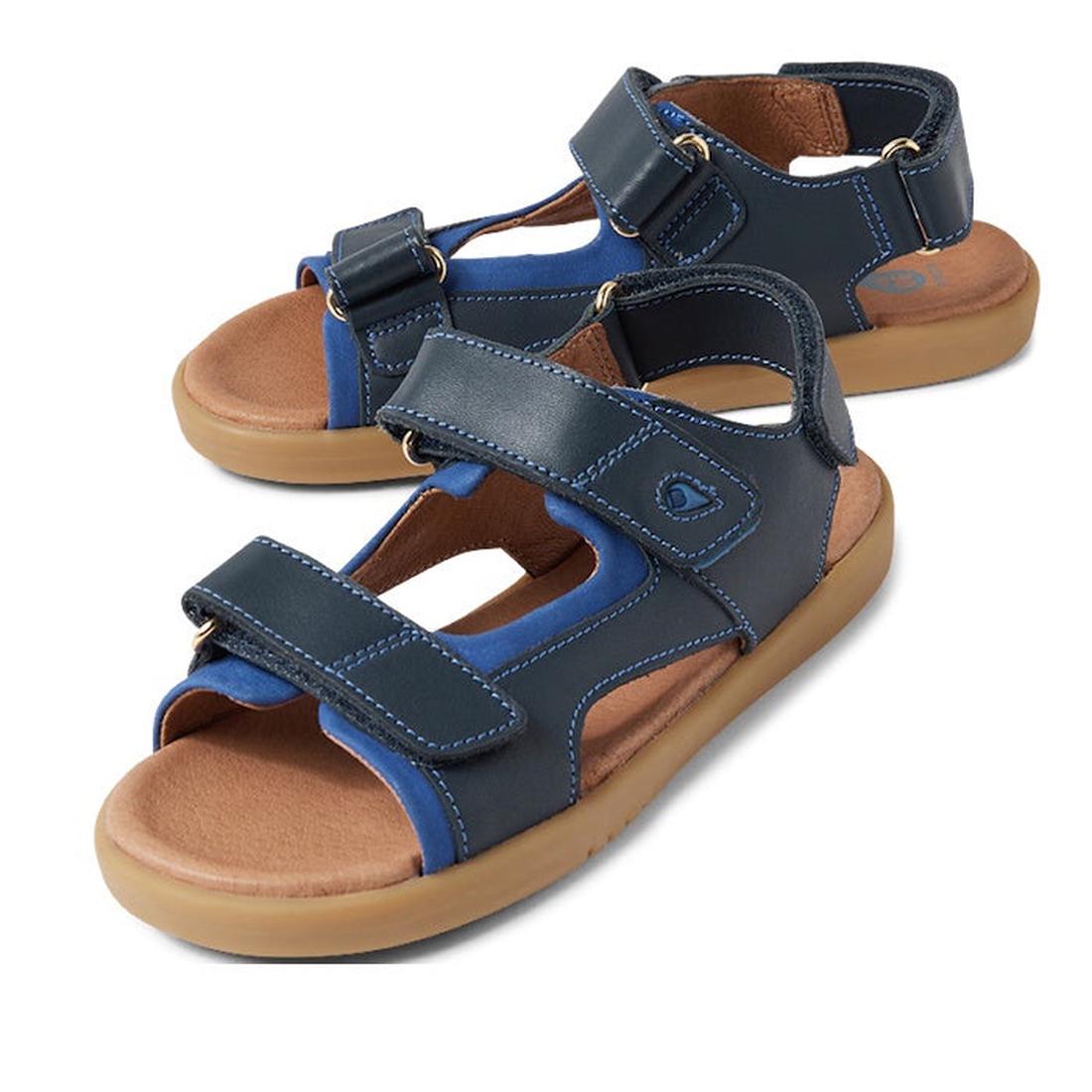 The Bobux Kid+ Plus Strand Navy Open Toe Sandal features adjustable Velcro straps, tan rubber soles, and a breathable design, providing comfort and casual style for kids.