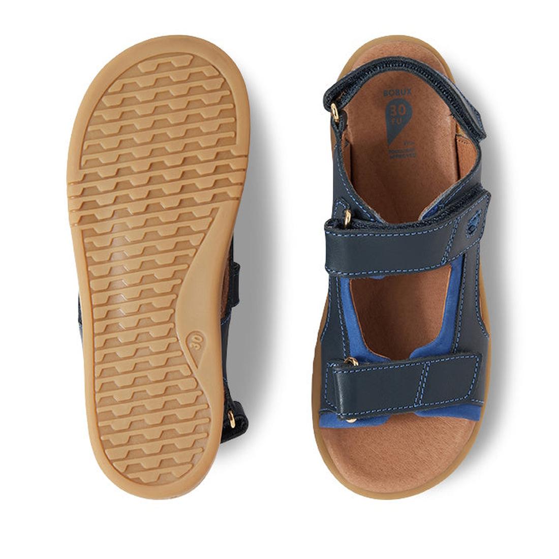 The Bobux Kid+ Plus Strand Navy Open Toe Sandal is shown from the top and bottom, highlighting its navy color, tan textured soles, breathable design, and adjustable velcro straps for kids., 9420068557048, 9420068557055, 9420068557062, 9420068557079, 94200