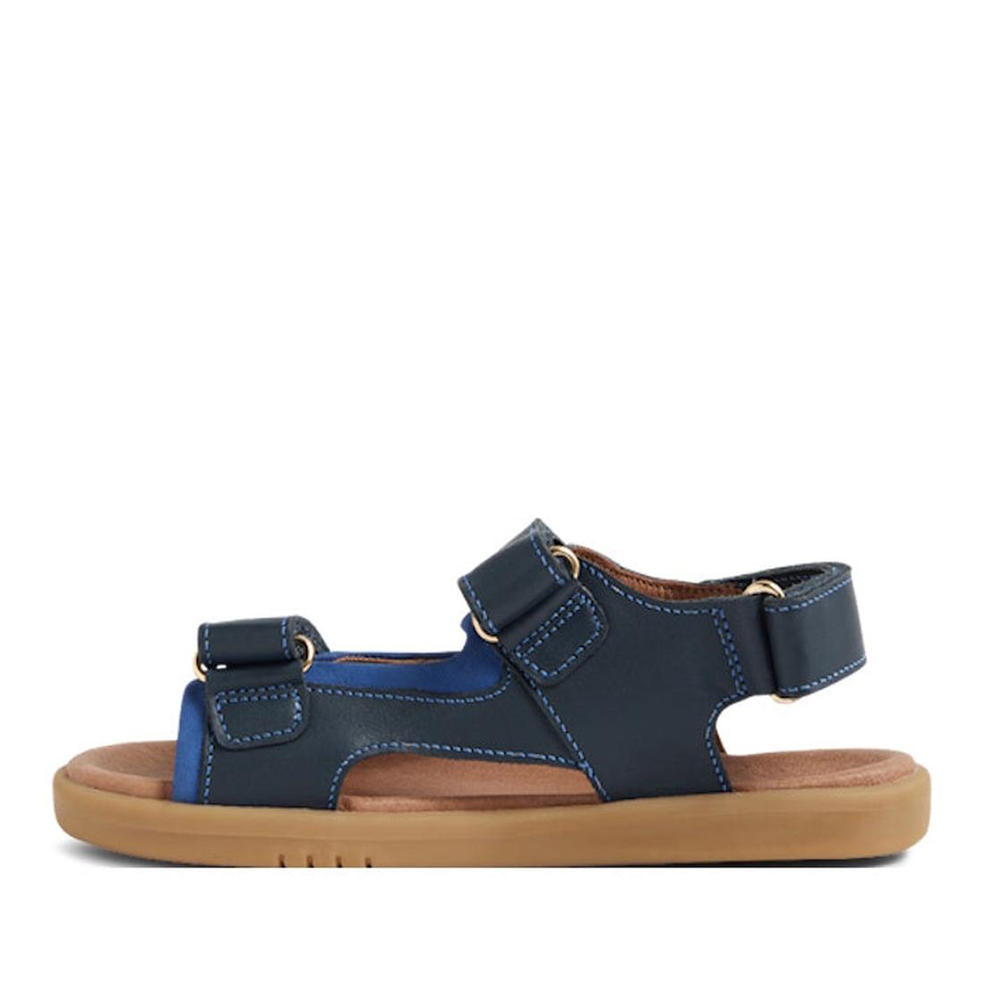 The Bobux Kid+ Plus Strand Navy Open Toe Sandal features adjustable straps, white stitching, a tan cushioned sole, and a breathable design for comfort—perfect for kids' casual wear., 9420068557048, 9420068557055, 9420068557062, 9420068557079, 942006855708