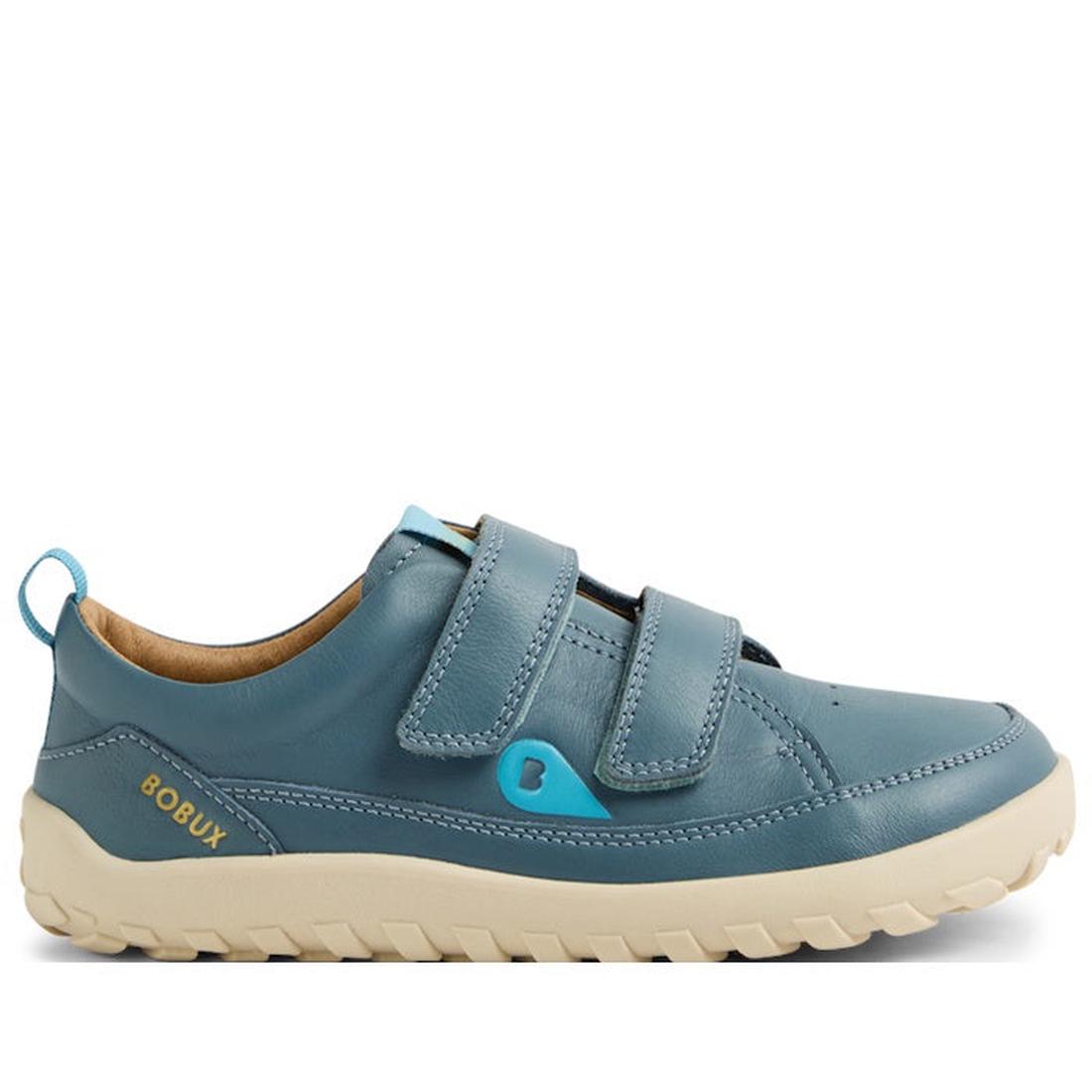 The Bobux Kid+ Dawn Leather Sneaker in Stormy Weather Blue features a barefoot-shaped toe box, beige rubber sole, two velcro straps, yellow BOBUX branding on the heel, blue pull tab at the back, and a small blue accent near the straps.