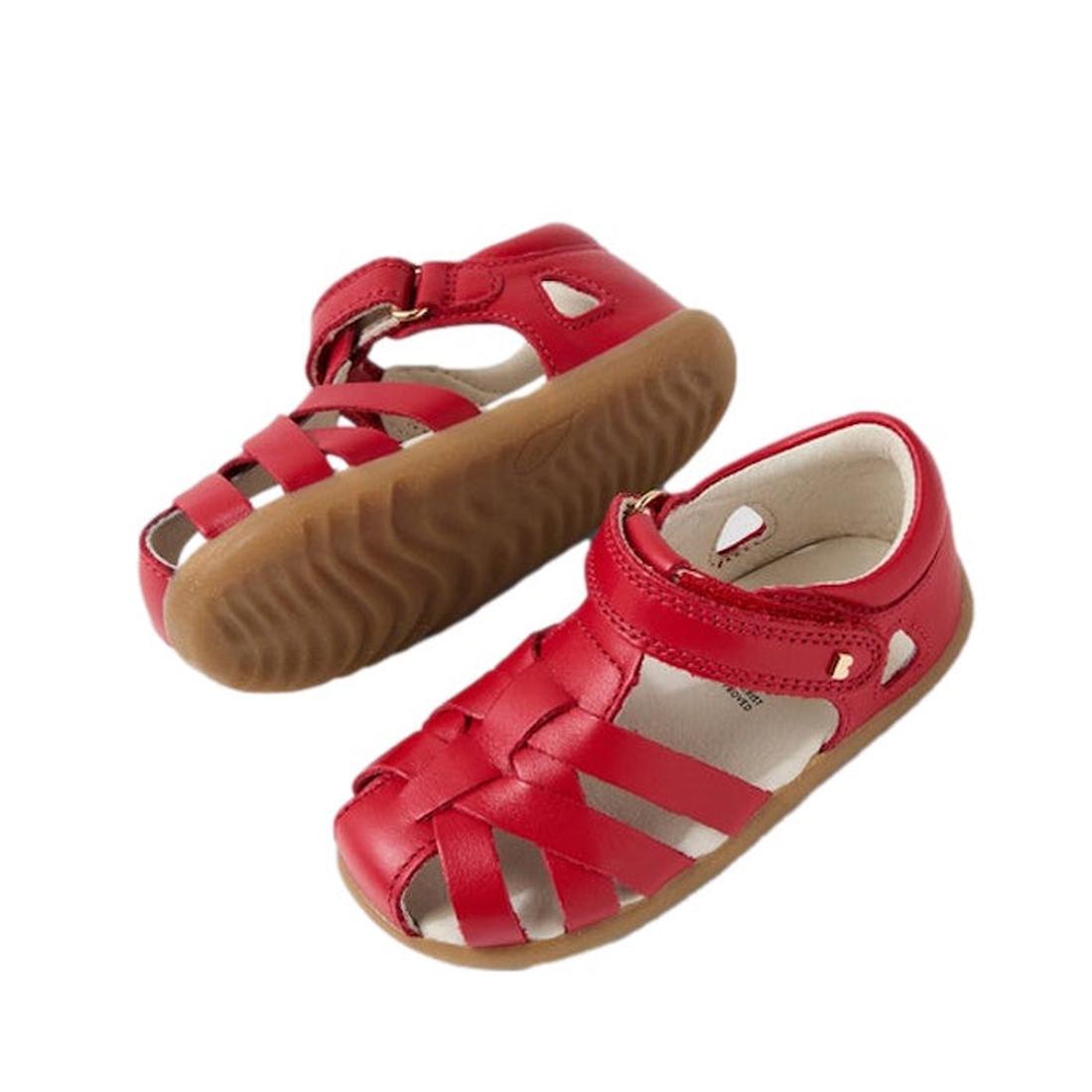 The Bobux Step Up Tropicana II Salsa Red Leather Sandal First Walker features red crisscross straps and tan rubber soles, ideal for pre-walkers, shown with one sandal upright and the other on its side.
