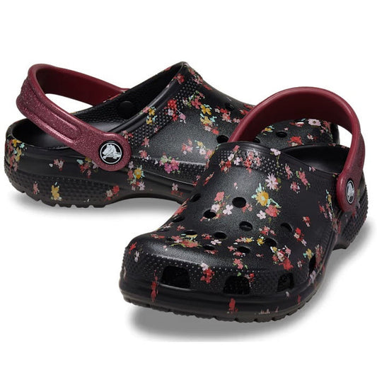 The Crocs Kids Youths Classic Clog K Ditsy Floral Black Multi Sandal, featuring ditsy floral graphics and maroon straps, is displayed against a white background.