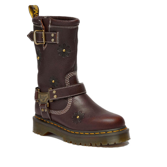 The Dr Martens Anistone Hi Flower Bex Grizzly Dark Brown is a mid-calf biker-style boot in brown leather, featuring floral embossing, two buckled straps, yellow stitching on a chunky treaded sole, and bold floral details.