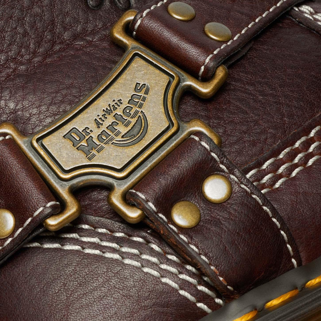 Close-up of the Dr Martens Anistone Hi Flower Bex Grizzly Dark Brown showing detailed white stitching, brass rivets, and a metal Dr. Martens logo plate on the brown leather strap., 52349, 190665773651, 190665773668, 190665773682, 52353, 52354, 52355, 5235