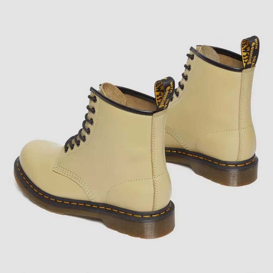 A pair of Dr. Martens 1460 Smooth Pale Olive 8 Up Leather Boots with black laces, black trim, yellow stitching on the soles, and branded heel loops are displayed on a light gray background., 190665531824, 190665531831, 190665531848, 190665531855, 19066553