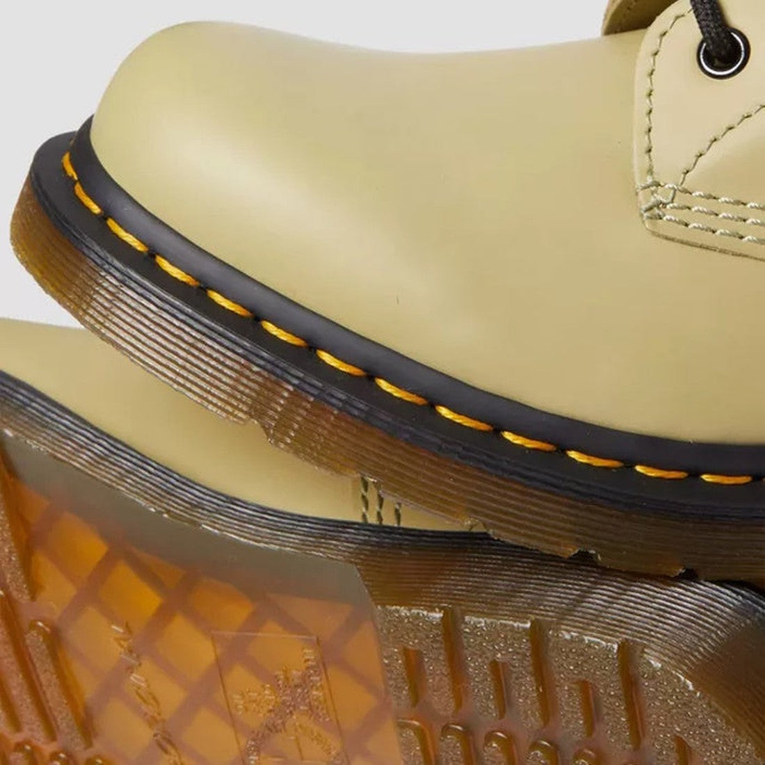Close-up of a Dr Martens 1460 Smooth Pale Olive 8 up Leather Boot in smooth leather with yellow stitching and a translucent brown rubber outsole, resting atop another boot with patterned tread., 190665531824, 190665531831, 190665531848, 190665531855, 1906
