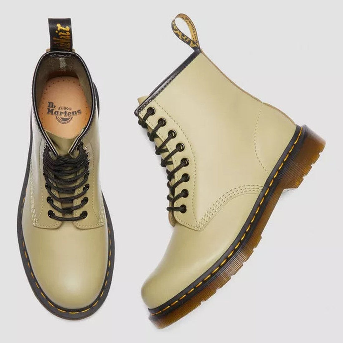 A pair of Dr Martens 1460 Smooth Pale Olive 8 Up Leather Boots with black laces, yellow stitching, and translucent brown soles—one boot upright, the other displaying the logo on the insole and heel loop., 190665531824, 190665531831, 190665531848, 19066553