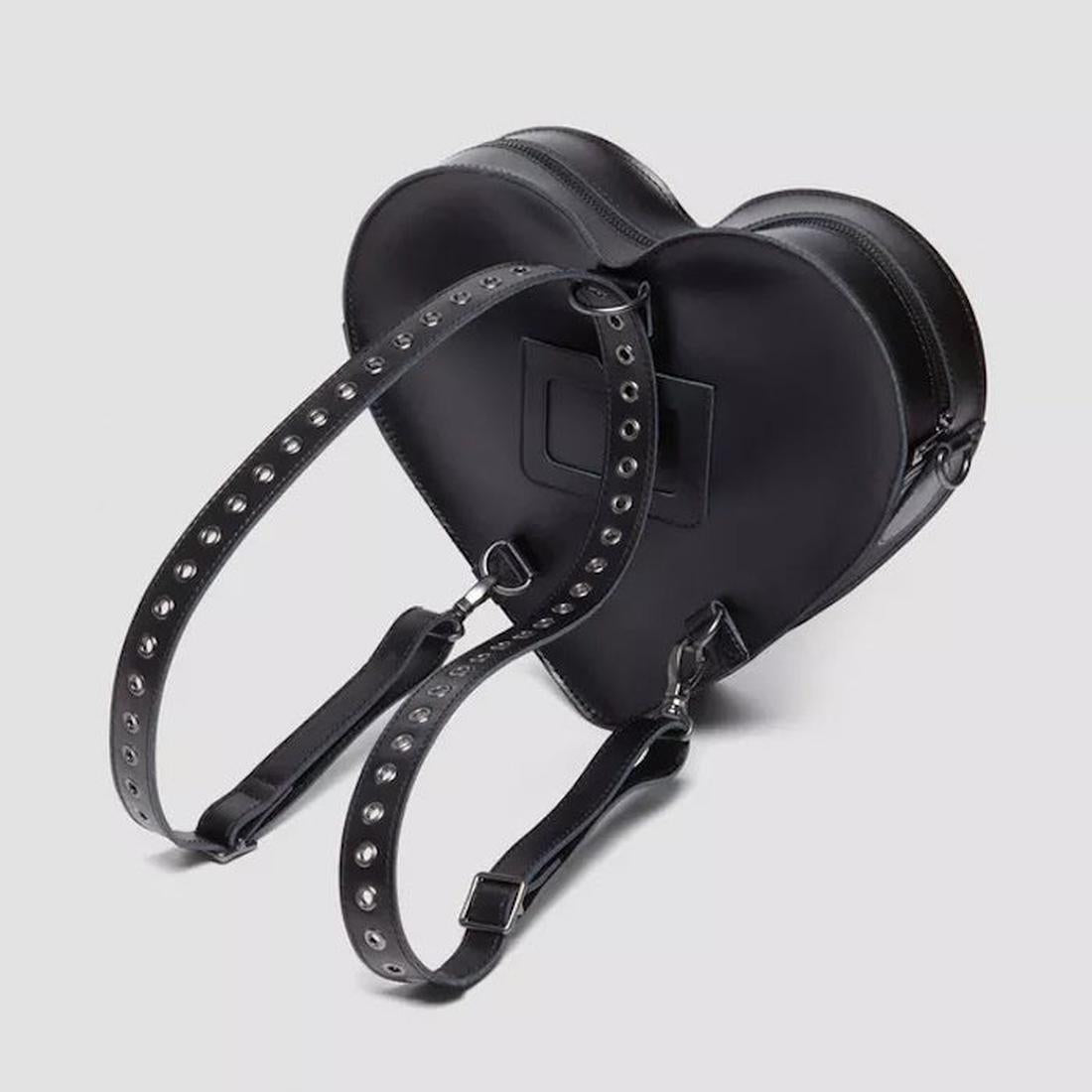 Dr Martens Heart Shaped Bag Hardware in classic black leather, with silver-studded adjustable straps, on a soft gray backdrop.  ksnz, 190665728408