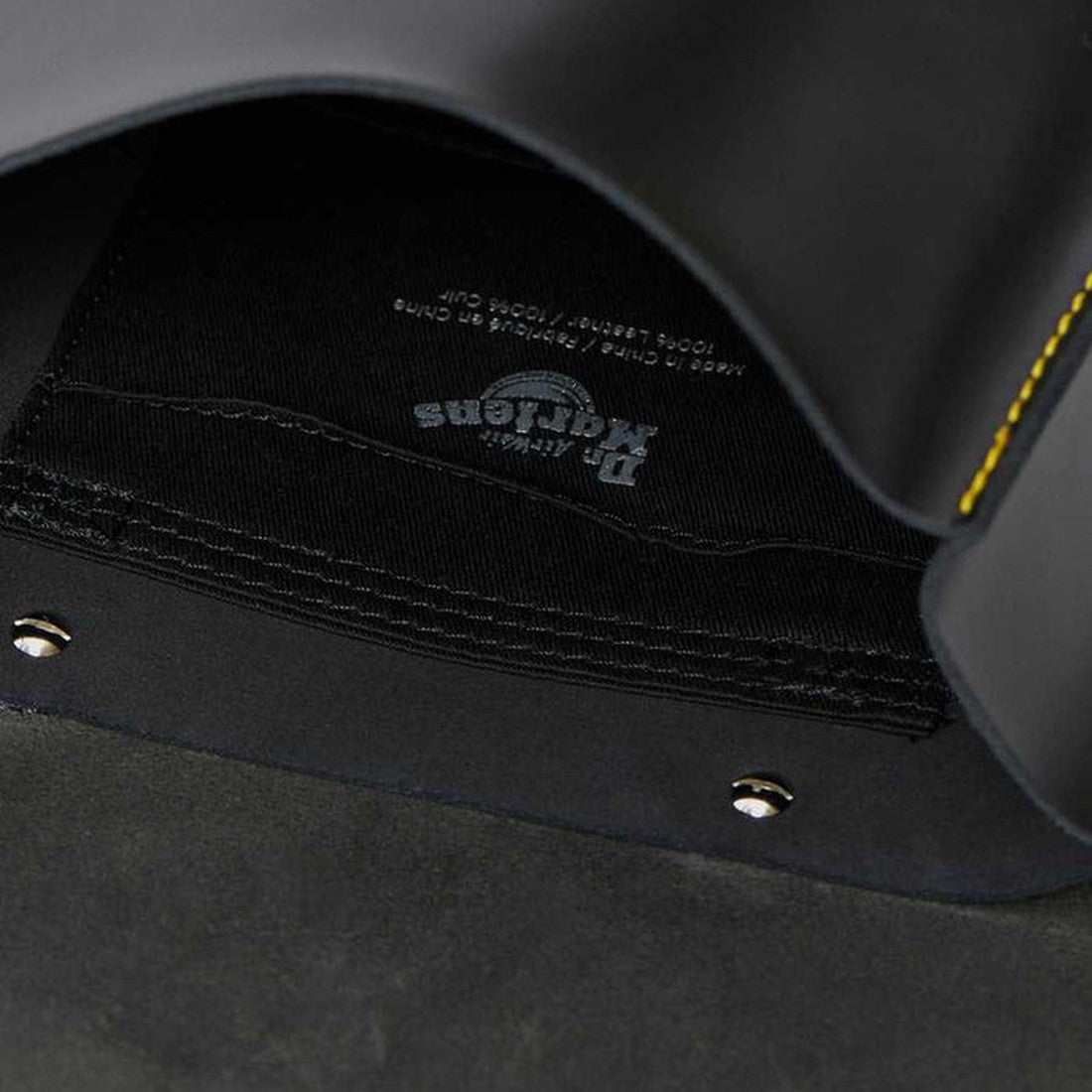 Close-up of the inside of a Dr. Martens shoe, featuring the brand logo, care instructions on a black insole, yellow stitching, and metal rivets—great to pair with the Dr Martens Mini Leather Backpack Black for a 90s-inspired look., 190665192032