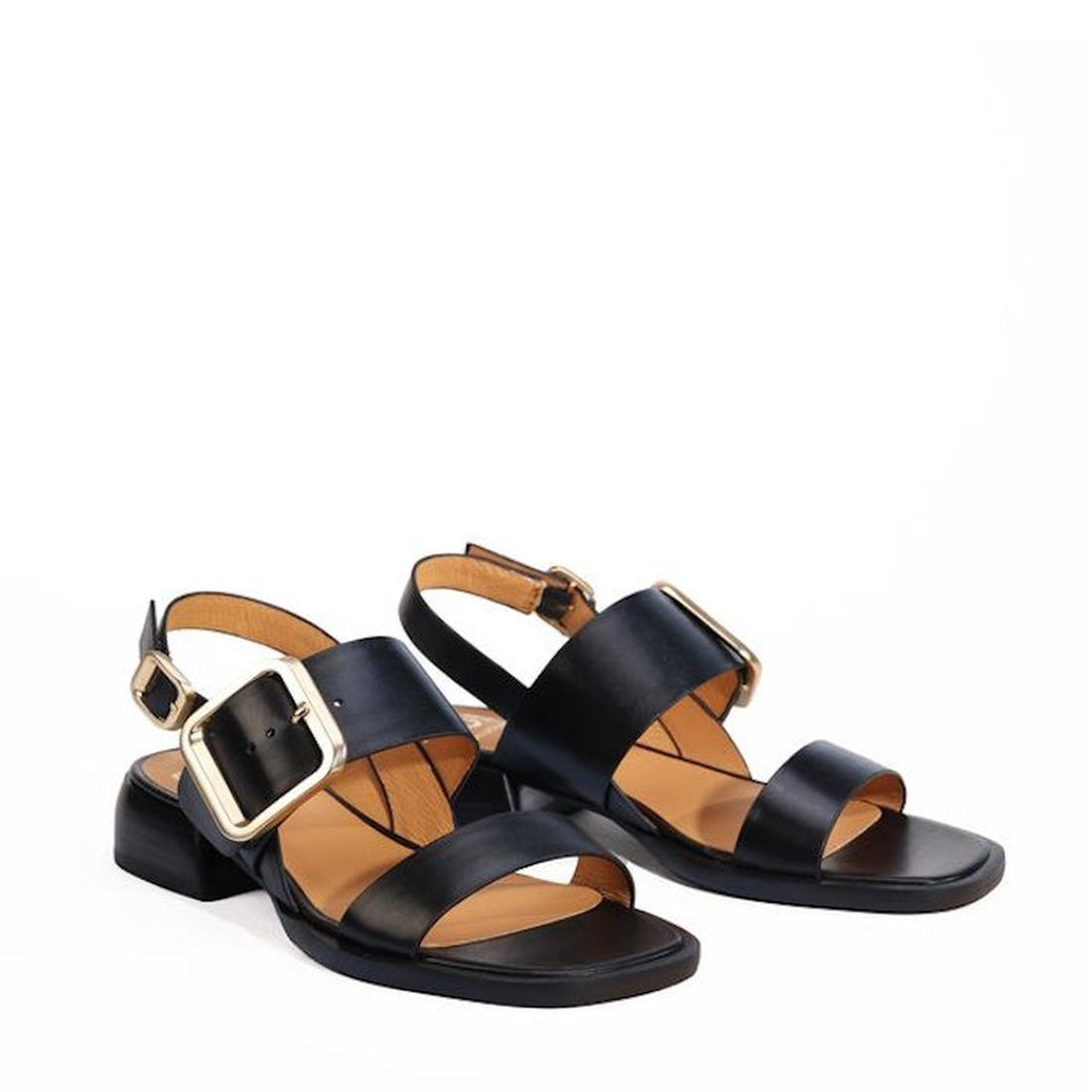 The EOS Ikam Women's Black Leather Low Heeled Sandal features wide crisscross straps, a back strap, tan insoles, large gold square buckles, and a low block heel, shown against a plain white background., 9321191304915, 9321191304922, 9321191304939, 9321191