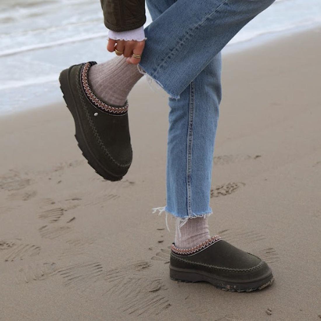 A parent strolls the beach in EMU NZ Women's Adventure Sharky Platform Scuff Slipper, dark olive sheepskin, platform sole, easy slip-on.  ksnz