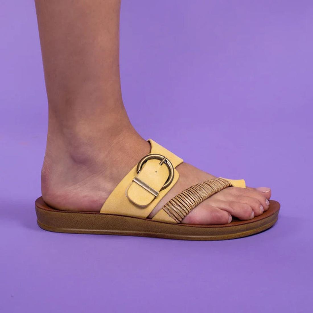 The Los Cabos Bria Sunset Light Flexible Sandal Jandal is a women's yellow thong sandal with a large buckle and fringe, shown on the foot against a solid purple background., 46928, 9321191296098, 9321191296104, 9321191296111, 9321191296128, 9321191296135,