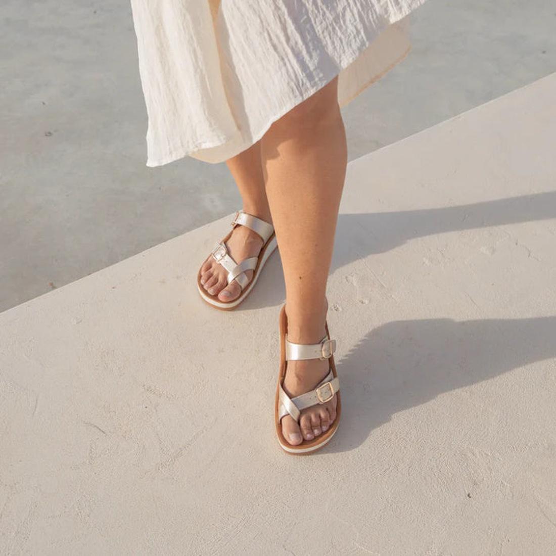 A person wearing a light, flowing skirt and Los Cabos Nins Champagne Adjustable Womens Summer Sandals with arch support stands on a sunlit, light-colored concrete surface., 46984, 9321191226729, 9321191226736, 9321191226743, 9321191226750, 9321191226767, 