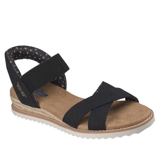 The Skechers Womens Bobs Desert Kiss Golden Lily Black SLIP IN features black strappy uppers, a tan Memory Foam footbed, beige espadrille-style sole, white ridged outsole, and a black ankle strap with soft patterned lining.