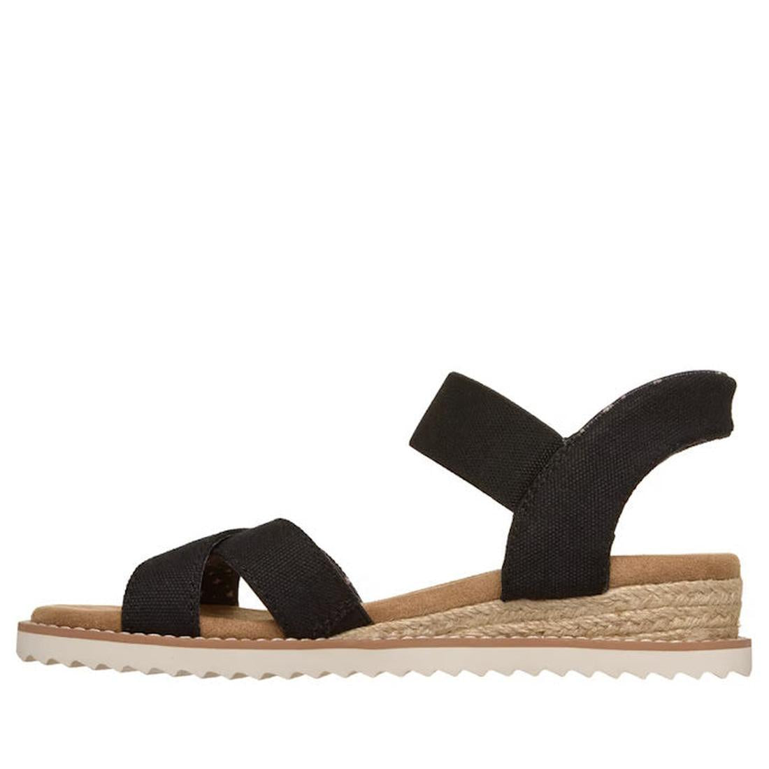Skechers Womens Bobs Desert Kiss Golden Lily Black SLIP IN: A black vegan slip-on sandal with crisscross fabric straps, ankle strap, tan Memory Foam footbed, braided jute-style midsole, and white ridged rubber outsole, shown in side profile on white backg
