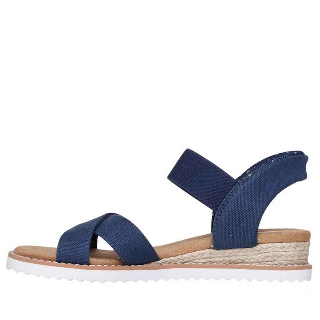 The Skechers Womens Bobs Desert Kiss Golden Lily Navy SLIP IN is a blue open-toe sandal with crisscross fabric and ankle straps, a tan Memory Foam footbed, woven espadrille-style midsole, and white ridged outsole, shown in side profile., 49030, 1987395587