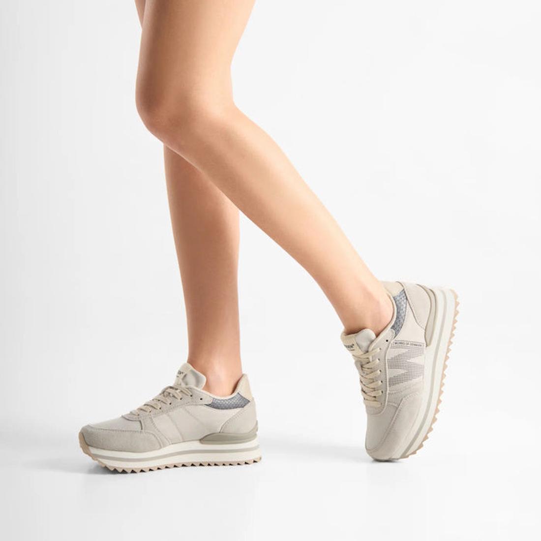 A person balances on one leg with the other bent, showcasing Woden Ronja Plateau Delpin Lace Up Sneakers made from sustainable materials. Only the legs and sneakers appear against a plain white background., 5713326692365, 5713326692372, 5713326692389, 571