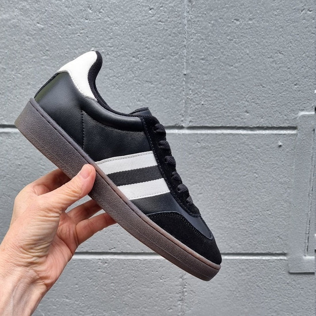 A caring hand displays the Alfie & Evie Attitude Suede Womens Sneaker, black and white with comfy memory sole and sporty white stripes.  ksnz, 9353738201500, 9353738201517, 9353738201524, 9353738201531, 9353738201548
