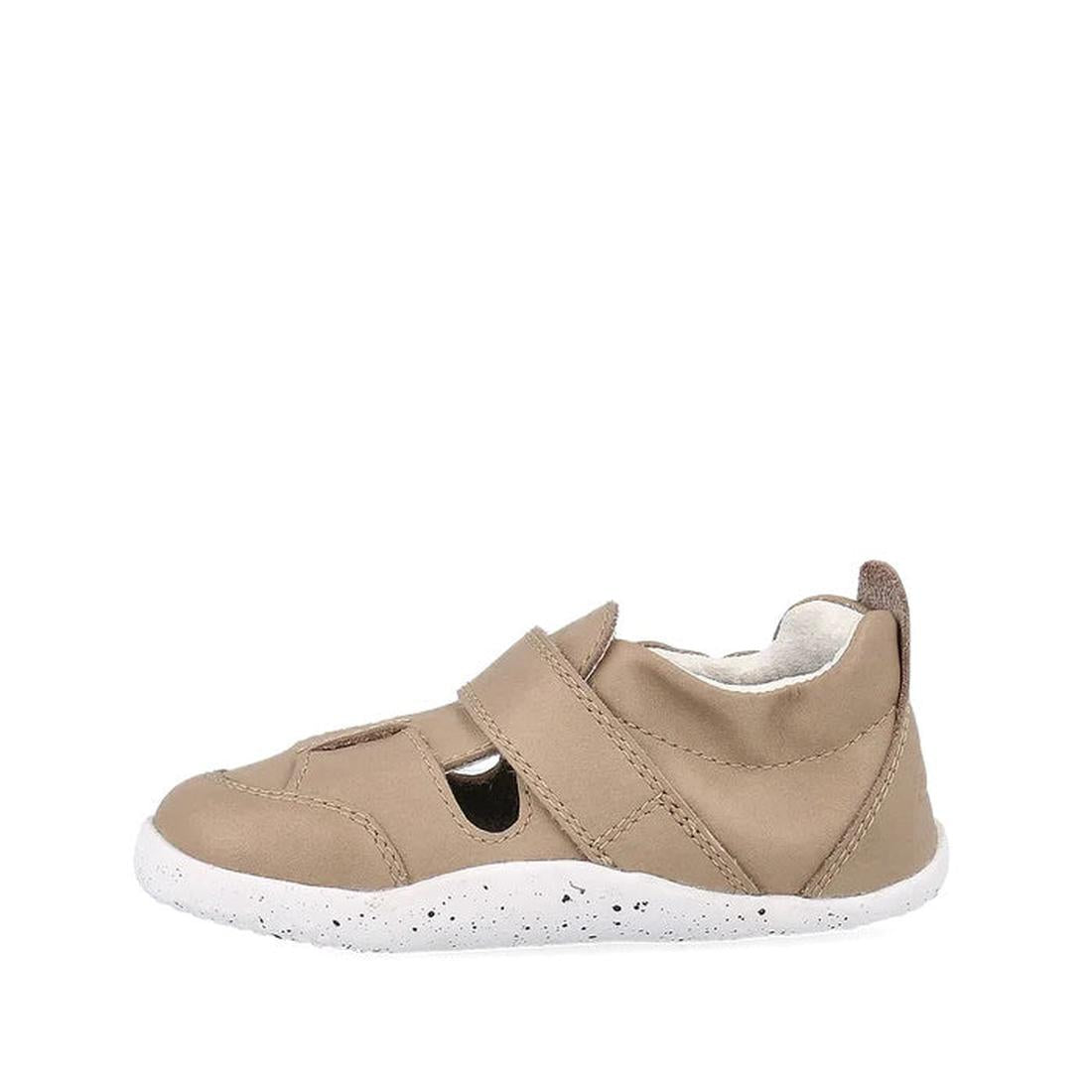 The Bobux XP Explorer Beau First Walker Sandal Atmosphere 502301 is a single tan sandal with cut-out sides, a Velcro strap, and a white speckled sole, shown in profile against a plain white background., 9420075784338, 9420075783690, 9420075786172, 9420075