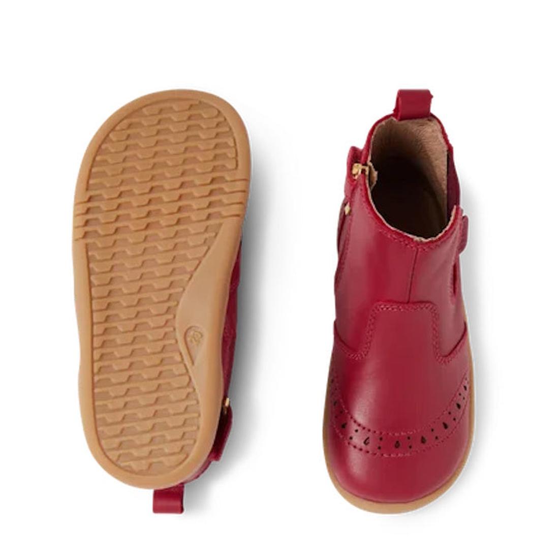 The Bobux Iwalk Billie Toddlers Leather Boot in Tibitan Red features tan rubber soles—one boot displays the tread from the bottom, while the other shows classic brogue-style details on the toe, inspired by traditional Billie boots., 9420068543799,
9420068