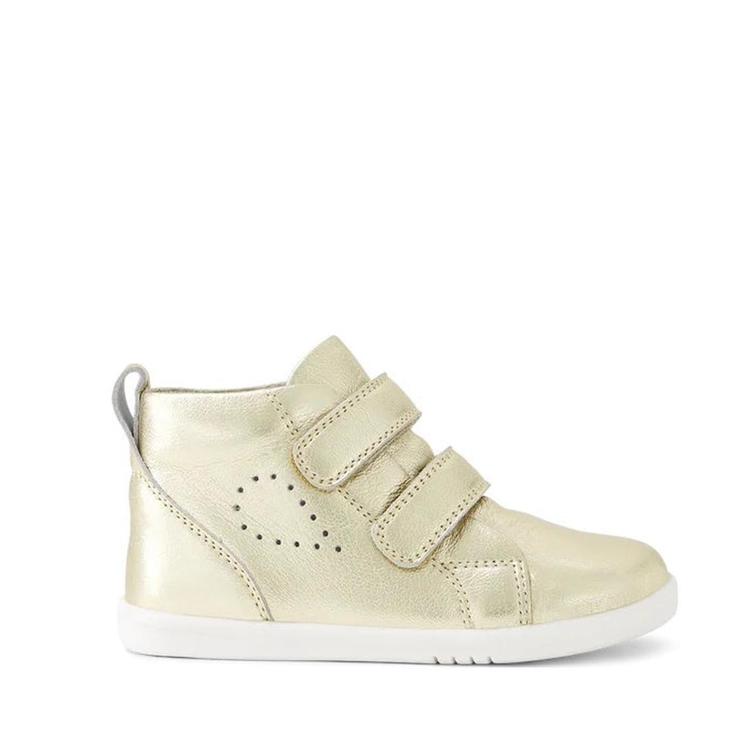 The Bobux IWalk IW Hi Grass Court Boot Pale Gold 650816 is a toddler's gold hi-top sneaker with double hook-and-loop fastening, a white sole, and side perforations. Displayed in profile against a white background.