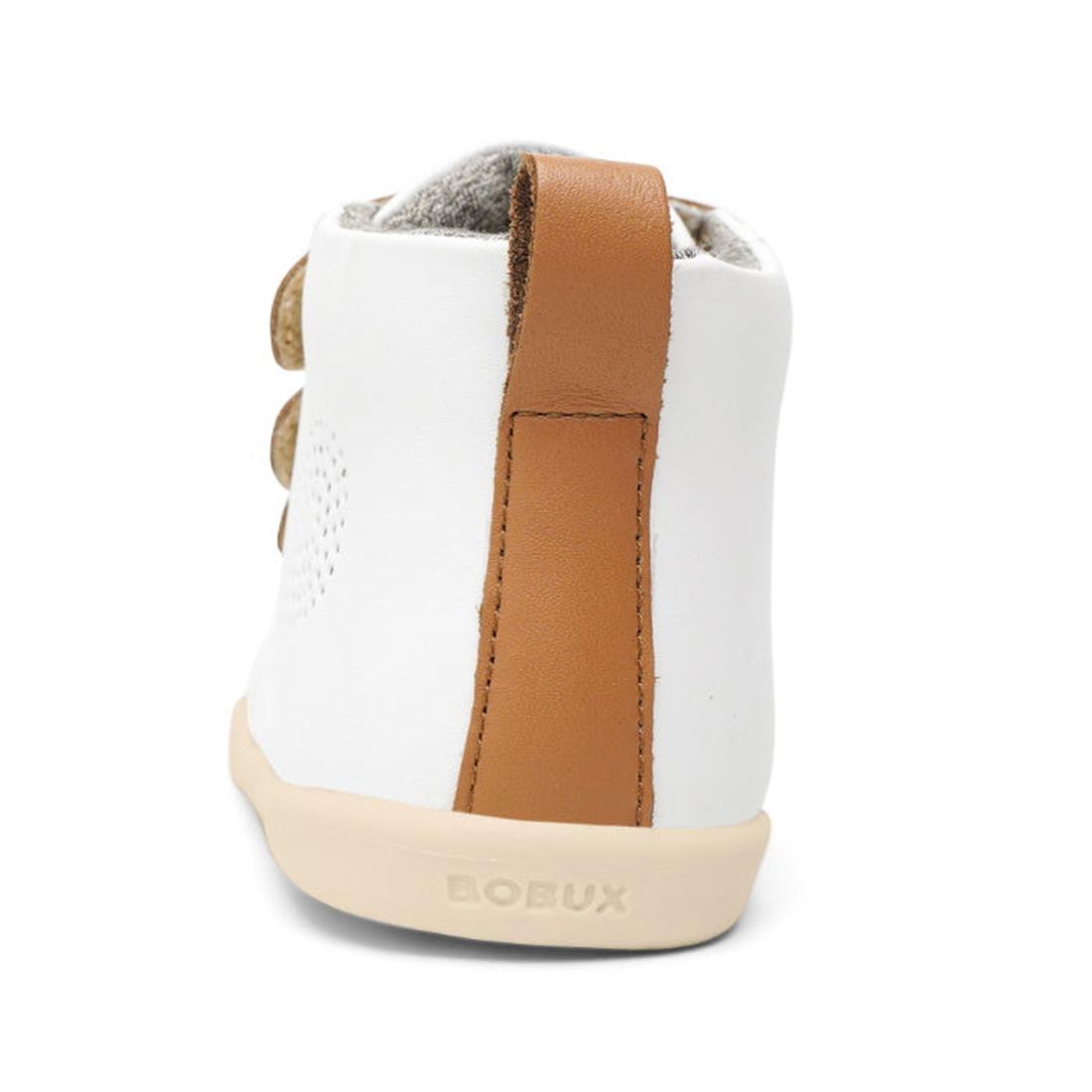 A close-up of the Bobux IWalk IW Hi Court Boot White Caramel shows a white baby shoe with a brown leather heel strap, beige sole, and BOBUX embossed on the heel, part of the Clearance collection., 9420071319701, 9420071319718, 9420071319725, 9420071319732