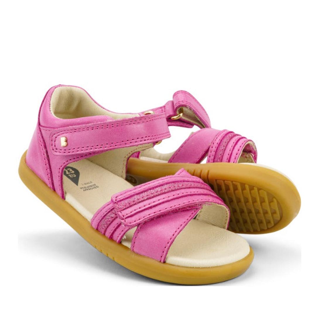 The Bobux iwalk IW Magic Girls Leather Sparkle Sandal in bright pink features leather uppers, tan rubber soles, and adjustable Velcro straps—ideal first-walker sandals. Open toe design shown against a white background.