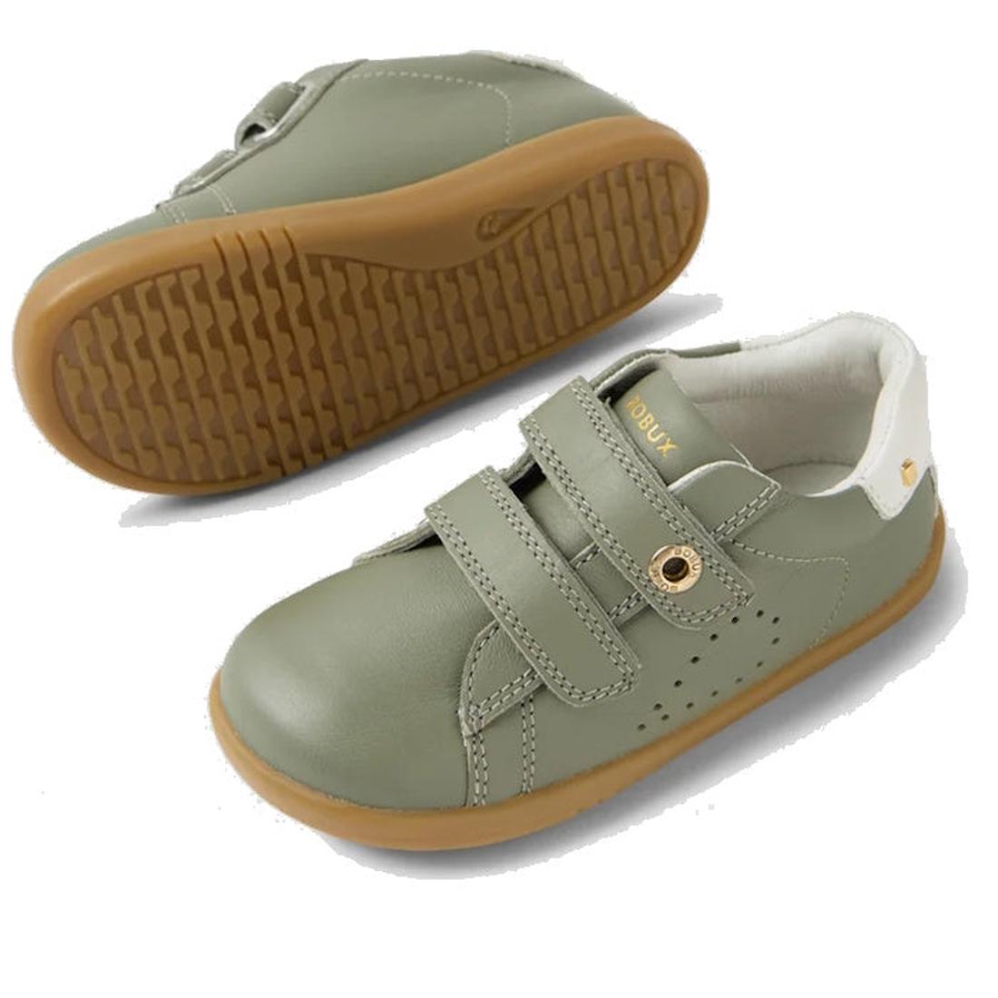 The Bobux IW Iwalk Maverick Leather Sneaker in Vetiver Green features kids' leather uppers, tan rubber soles, white heel detail, perforated sides for breathability, and double adjustable straps. One shoe is shown side-on; the other displays the textured s
