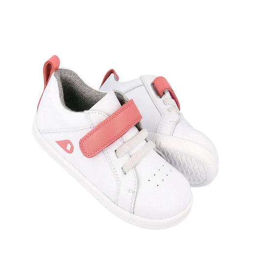 The Bobux Kids IWalk IW Pace Sneaker White Coral 650402 is a pair of white leather unisex sneakers with pink velcro straps, coral accents, perforated toes, and white soles, shown on a plain white background.