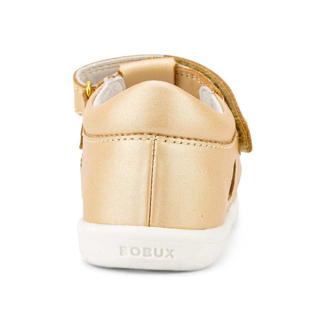 The Bobux Iwalk IW Tropicana II Sandal 638311 in Pale Gold is shown from the back, featuring a white sole, embossed BOBUX branding on the heel, and a visible Velcro strap. Made from Quick Dry Leather—ideal for active kids., 9420068529946, 9420068529953, 9