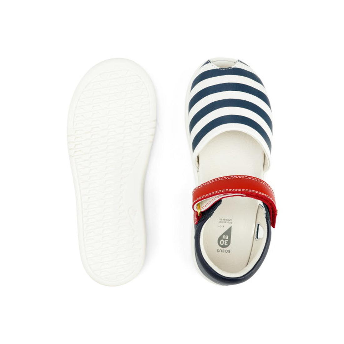Top view of the Bobux Kid + KP Twist Open Toe Sandal Navy, showcasing premium leather in navy and white stripes, a red strap with gold buckle, closed back heel support, and a white sole. The left shoe is upright; the right shows its tread., 9420068530331,