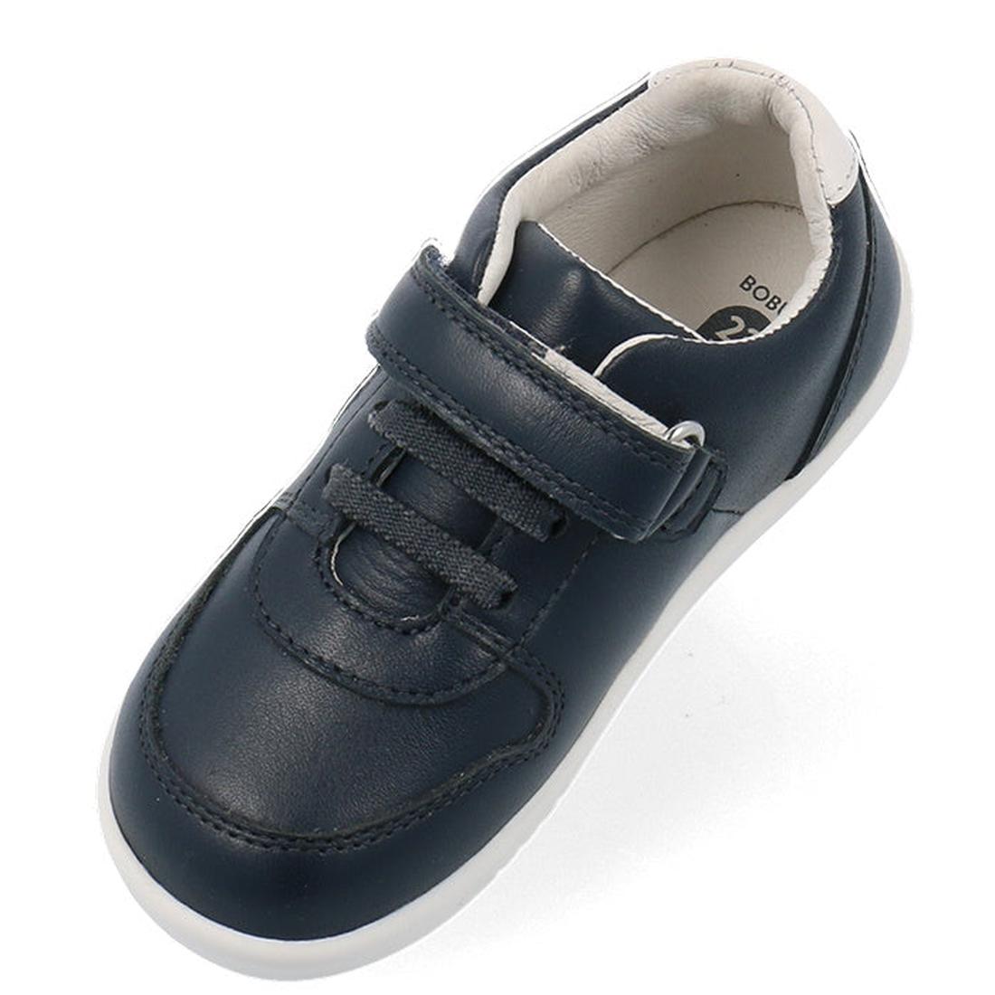 An angled top view shows a single Bobux Kids IWalk IW Comet Sneaker in navy/white with a white sole, hook-and-loop strap, and elastic laces—a stylish leather shoe choice for kids., 9420075706118, 9420075706125, 9420075706132, 9420075706149, 9420075706156