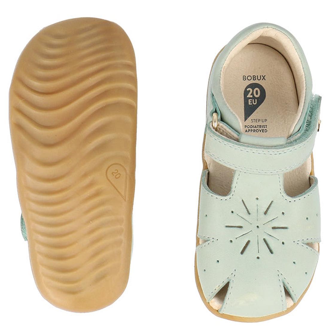 The Bobux Step Ups Compass Mist Aqua 734905 Toddler Girls Sandal features light blue closed toes, tan rubber soles, a textured sole bottom, and a cutout starburst design—perfect as first walker shoes., 9420075708594, 9420075708600, 9420075708617, 94200757