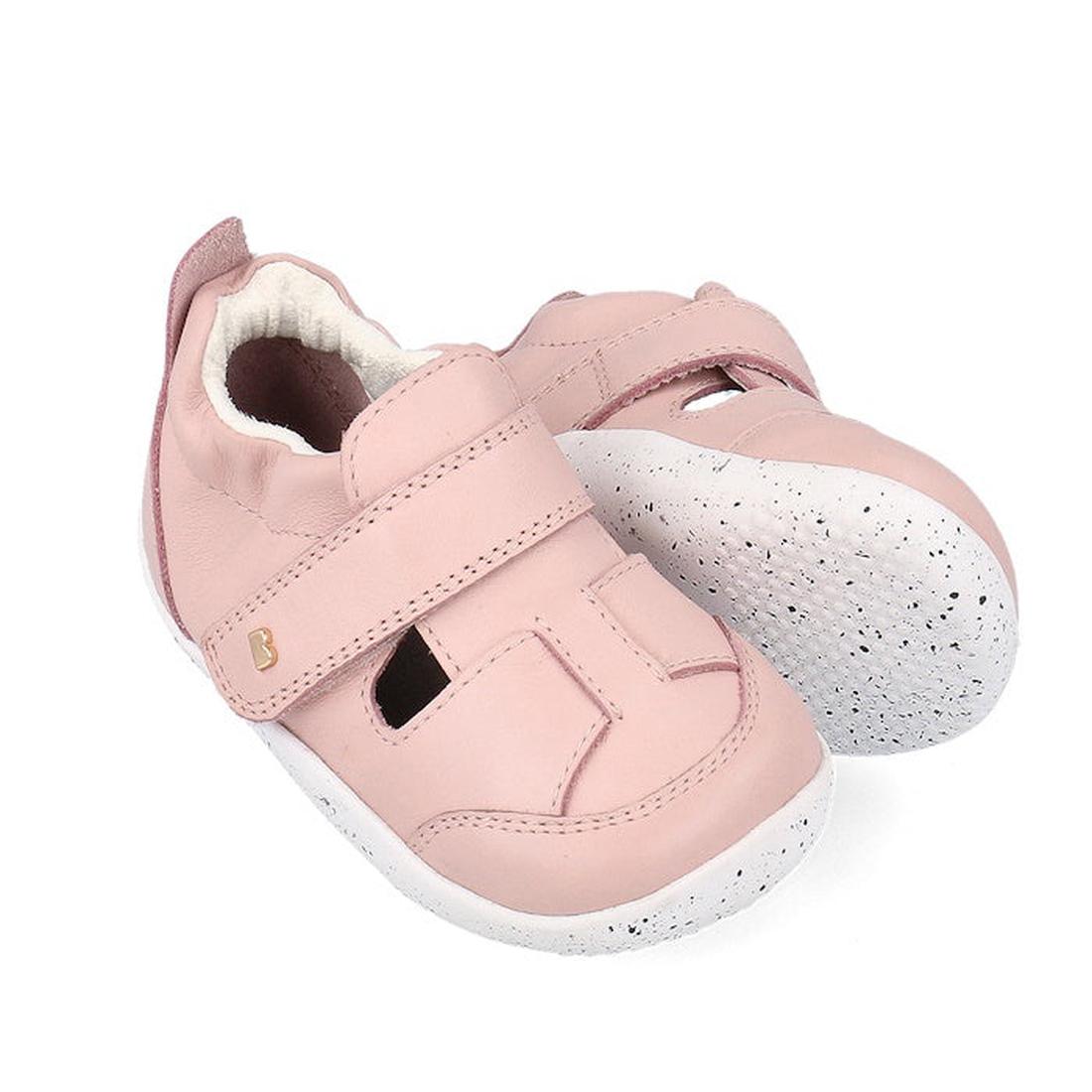 The Bobux XP Explorer Beau First Walker Sandal Blossom Pink 502305 features light pink uppers, velcro straps, white flexible soles, a gold B logo, and cute cut-out details on top. Displayed against a white background.