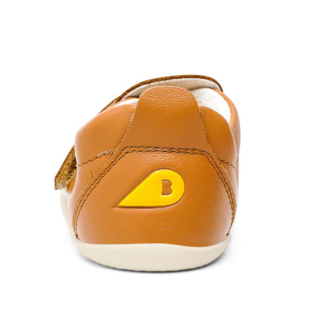 The Bobux Xplorer Go Caramel Tan First Walker 501037 is a brown leather baby shoe with a yellow "B" accent on the heel and a flexible sole—perfect as one of your baby's first walking shoes., 9420071319039, 9420071319046, 9420071319053, 9420071319022