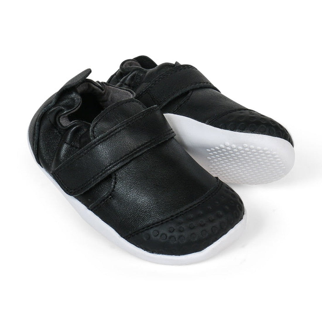 The Bobux Explorer Go Black/White 501001B toddler shoes feature black uppers, white textured rubber soles, and Velcro straps for comfort and support, shown against a white background.