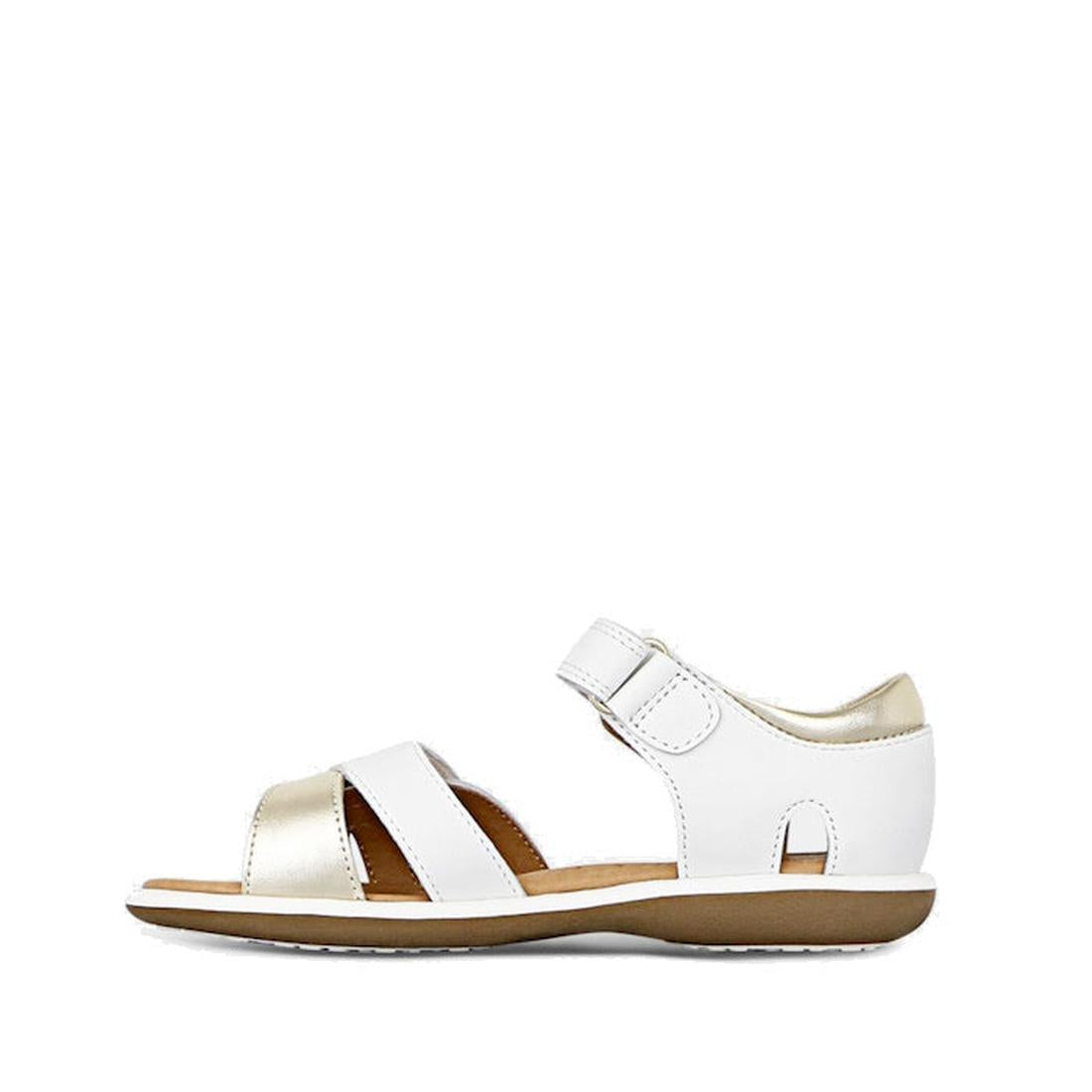 The Clarks Girls Pippa White Leather Sandals (E width) feature a white and gold leather upper, open toe, adjustable hook-and-loop ankle strap, and flat brown sole, shown in profile on a white background., 9336078233325, 9336078233349, 9336078233363, 93360