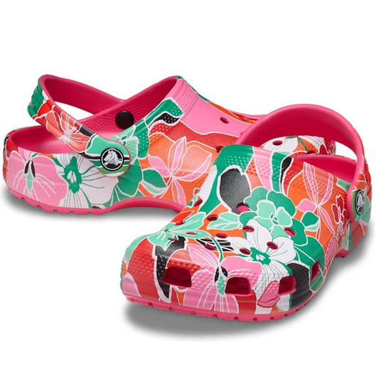 The Crocs Kids Youths Classic Clog K Woodcut Floral Print features a vibrant pink, red, green, and white floral pattern, adjustable heel strap, toe ventilation holes, Crocs Comfort, and can be customized with Jibbitz charms.