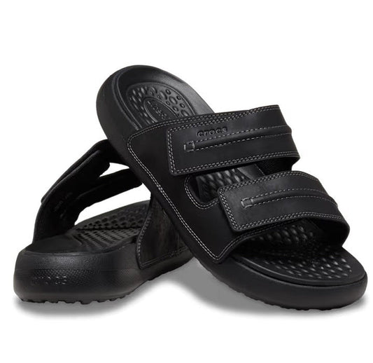 A pair of Crocs - Mens Yukon Vista II LR Sandals Slide Black with two adjustable velcro straps and textured footbeds; one sandal stands upright while the other is angled in front.