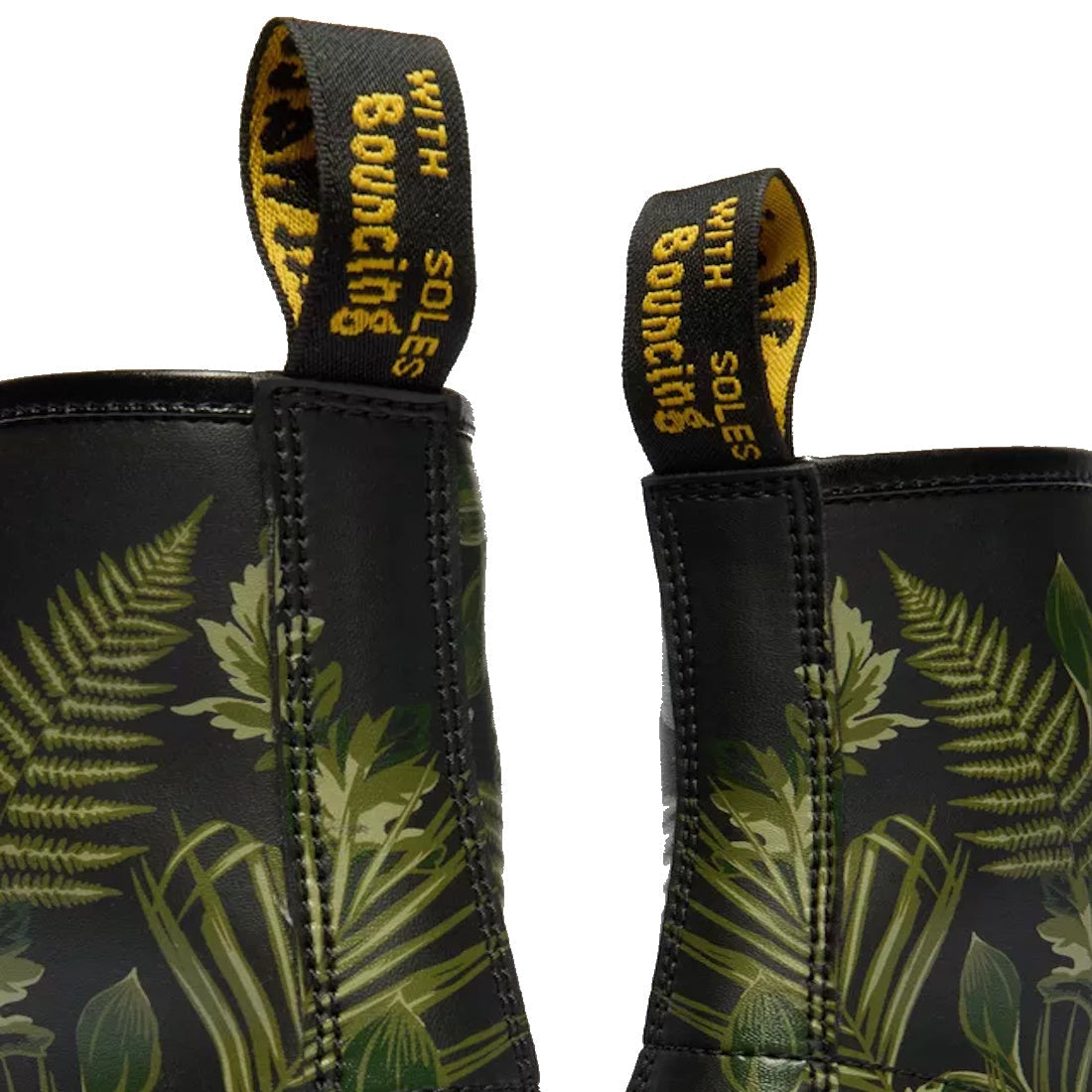 Close-up of two 1460 Dr Martens Smooth EverGreen Leather 8 Up Boots featuring green leaf patterns on a black background, yellow and black “WITH BOUNCING SOLES.” pull tabs, and sturdy Goodyear-welted construction.