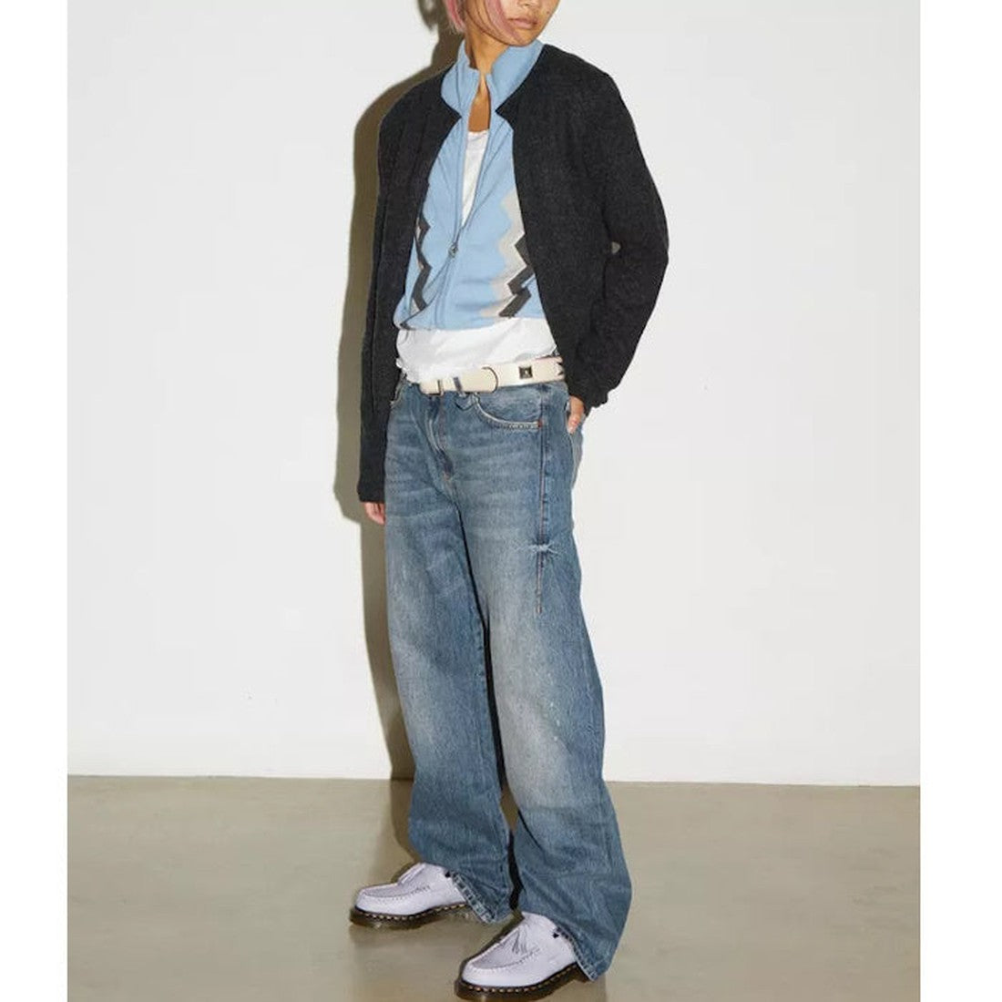 A person stands against a white wall wearing a black jacket, blue zigzag shirt, baggy blue jeans, a white belt, and Dr Martens Adrian Lavender Frost Virginia Leather Tassel Loafers. Their face is partially out of frame., 41118, 190665677430, 190665677447,